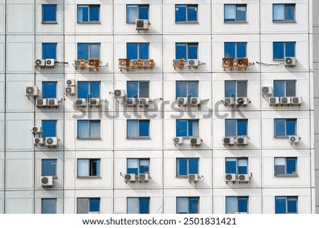 Multiple air conditioning units mounted on the facade of building with numerous windows, cooling systems in urban architecture. Air conditioning units on exterior building wall.