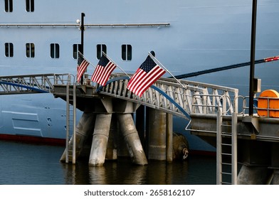 multiple american flags fly from a pier next to a large white cruise ship on shore