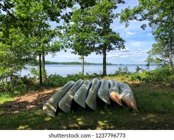 Multiple Canoes laying on the beautiful green grass surrounded by trees.
