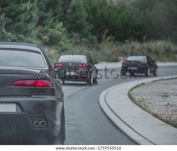 Multiple cars driving\
together in a column on a cold rainy day. Car enthusiast gathered\
and going for a road trip. Back view of a modified car with four\
exhausts