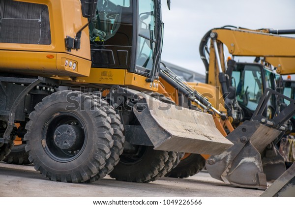 Multiple cars, excavators,
trucks, loaders, concrete mixers and construction machinery in
large parking lot in industrial territory, next to concrete and
asphalt factory