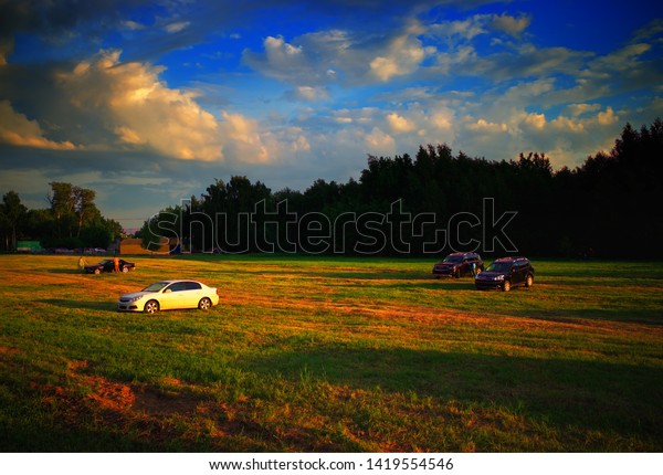 Multiple cars meeting sunset on dramatic\
countryside field\
background