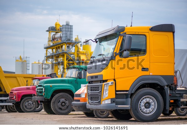 Multiple cars, trucks, loaders,
concrete mixers and construction machinery in large parking lot in
industrial territory, next to concrete and asphalt factory 
