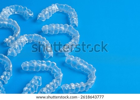 Multiple clear dental aligners are displayed on a blue surface. These orthodontic devices are designed for teeth alignment, showcasing their transparent design.