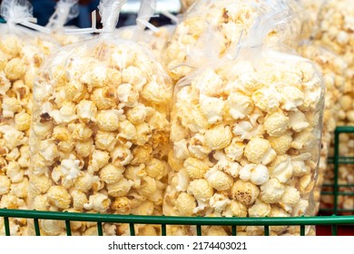 Multiple Clear Plastic Bags Of Confection Containing Caramel Corn Popcorn,for Sale By A Street Vendor. The Sweet Tasty Snack Of Candy Corn Is Stacked In A Green Wire Basket At A Farmer's Market Stall 