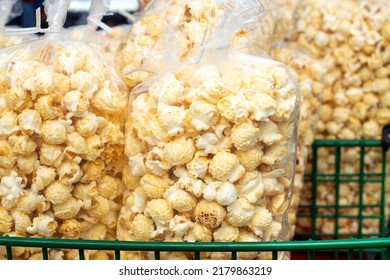 Multiple Clear Plastic Bags Of Confection Containing Caramel Corn Popcorn, For Sale By A Street Vendor. The Sweet Tasty Snack Of Candy Corn Is Stacked In A Green Wire Basket At A Farmer's Market Stall