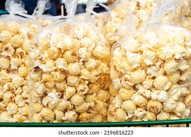 Multiple clear plastic bags of confection containing caramel corn popcorn,for sale by a street vendor. The sweet tasty snack of candy corn is stacked in a green wire basket at a farmer's market stall 