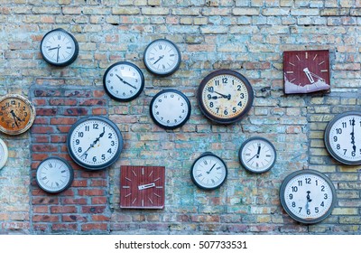 Multiple Clock. Plurality Of The Different Clocks On The Old Brick Wall.