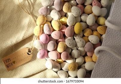 Multiple colorful chocolate Easter eggs with gift tag in gift bag on canvas. Flat lay, top up view. Easter, spring symbol