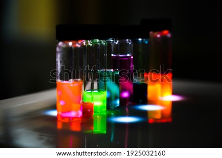 Multiple colourful analytical sample in glass vial in an inorganic chemistry laboratory experiment on the UV light by a woman scientist