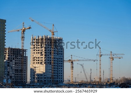 Multiple construction cranes working on modern residential buildings against a clear blue sky, showcasing urban development and growth in progress