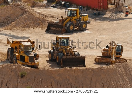 Multiple construction and mining vehicles working inside an active open pit quarry. Heavy machinery performs excavation and material transport across industrial extraction site.