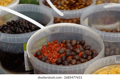 Multiple containers filled with different types of olives and spices are set up at a busy local market