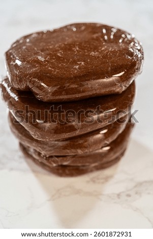 Multiple discs of Chocolate Gingerbread Cookie Dough wrapped in plastic wrap, stacked and ready to chill. These dough discs make it convenient to shape cookies for holiday baking.