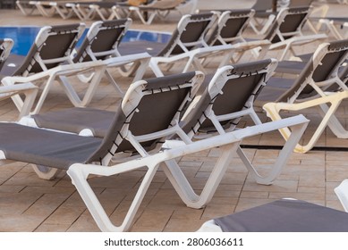 Multiple empty deckchairs are neatly arranged in rows on a paved terrace by the water. The repetitive pattern creates a clean geometric composition emphasizing high season readiness or offseason silence.