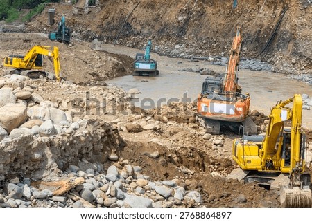 Multiple excavators operating in a river channel to repair erosion damage, moving rocks and soil for flood control and land stabilization.