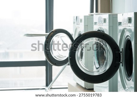 Multiple front-loading washing machines arranged neatly beside a large window in a modern laundry space