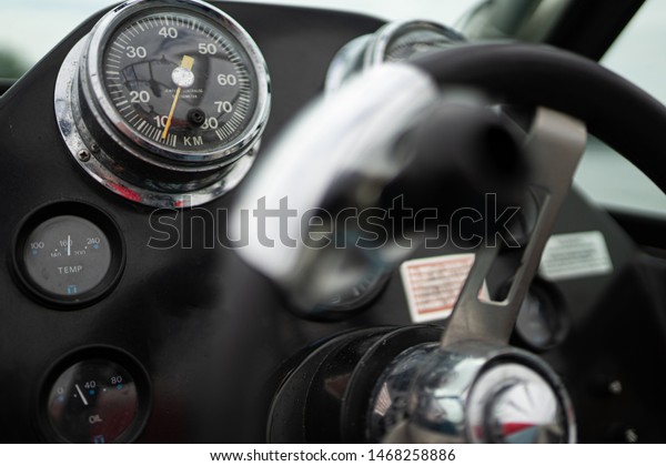 Multiple gauges and a\
steering wheel in the dashboard in a cockpit of a speed boat /\
motor boat on a river.