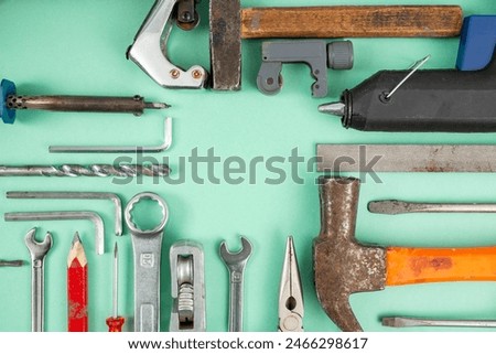 Multiple hand tools arranged on green background, with empty square copy space in the middle
