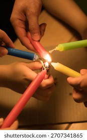 Multiple hands gather around a small flame as they ignite brightly colored candles using a single lit candle evoking the festive spirit of Christmas