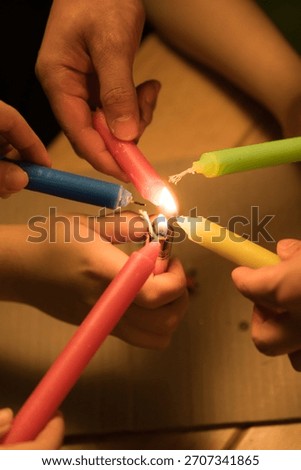 Multiple hands gather around a small flame as they ignite brightly colored candles using a single lit candle evoking the festive spirit of Christmas