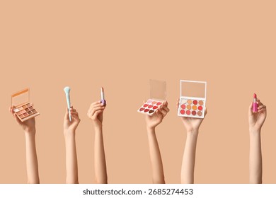 Multiple hands holding various makeup products including eyeshadow palettes, lipsticks, and a brush on a neutral background