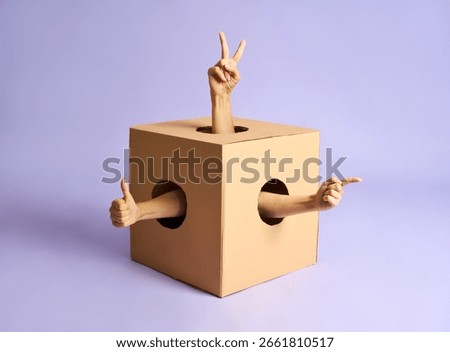 Multiple hands making peace, thumbs up, and pointing gestures from holes in cardboard box.