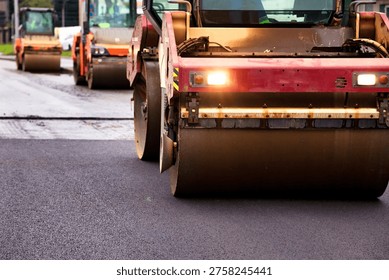 Multiple heavy road rollers compact fresh asphalt concrete pavement on a bustling city street. Copy ad text space