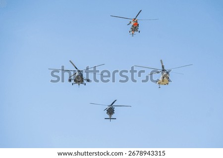 Multiple helicopters performing coordinated maneuvers in a clear blue sky during an air show