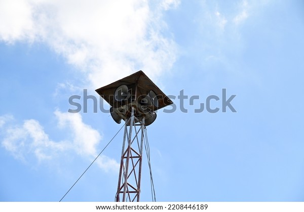 Multiple horn speakers on the tower of steel\
columns there is a roof covering with blue sky and white clouds\
background for distributing press releases to the people in the\
village at Thailand.