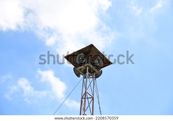 Multiple horn speakers on the tower of steel\
columns there is a roof covering with blue sky and white clouds\
background for distributing press releases to the people in the\
village at Thailand.