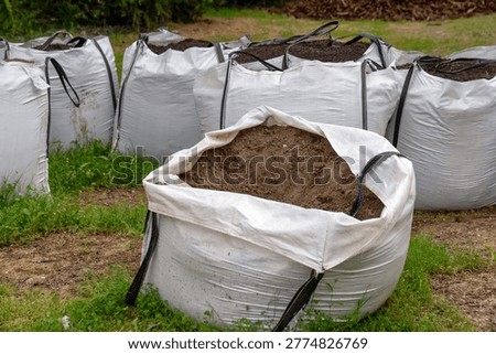Multiple large white bulk bags filled with brown soil for gardening and construction use