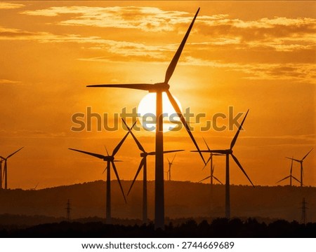 Multiple large wind turbines spinning gracefully against a dramatic and vibrant orange sunset sky in a green renewable energy project
