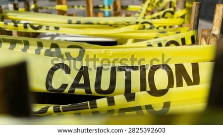 Multiple layers of bright yellow caution tapes with bold black lettering are strung across wooden posts, indicating danger, restriction, or safety warnings