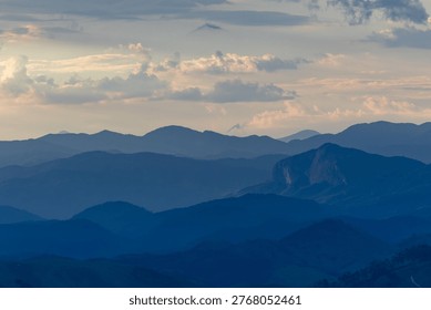 Multiple layers of mountains extend across the horizon under a softly lit sky at dusk. The overlapping silhouettes create depth and atmosphere, offering a calm and expansive natural scene suitable for concepts related to travel, serenity, scale, and the natural environment.
