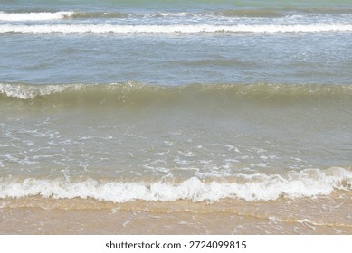 Multiple layers of turquoise ocean waves roll rhythmically toward a golden sandy beach, capturing the dynamic motion of surf meeting shore. Crisp white foam accents highlight each successive breaker under clear skies. High-resolution seascape stock photo perfect for ocean, relaxation, nature, or coastal lifestyle themes.
​