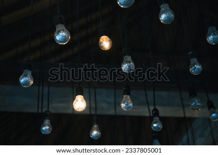 Multiple light bulbs hanging from the ceiling. Brainstorming, invention. creativity, ideation, and solutions symbol image. Idea finding workshop. Dark background with multiple light bulbs in front.  