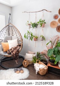 Multiple Macrame Plant Hangers With Indoor Houseplants And Pot Planters Are Hanging From A Metal Pole. Boho Basket Wall Decor And Wicker Egg Chair Are Use To Add Character To The Cozy Bohemian Room.