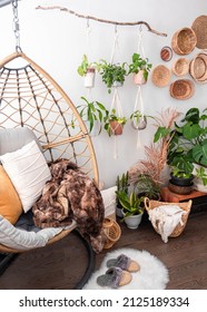 Multiple Macrame Plant Hangers With Indoor Houseplants And Pot Planters Are Hanging From A Metal Pole. Boho Basket Wall Decor And Wicker Egg Chair Are Use To Add Character To The Cozy Bohemian Room.