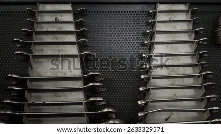 Multiple metal wrenches arranged in rows on a tool board in a mechanic workshop.