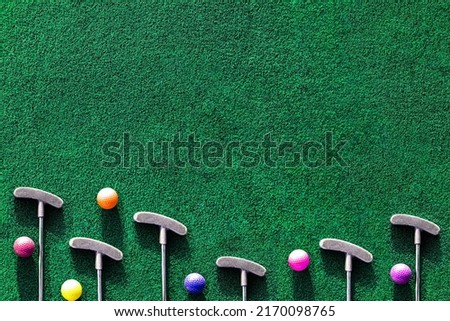 Multiple mini golf clubs and balls on putting green background with copy space