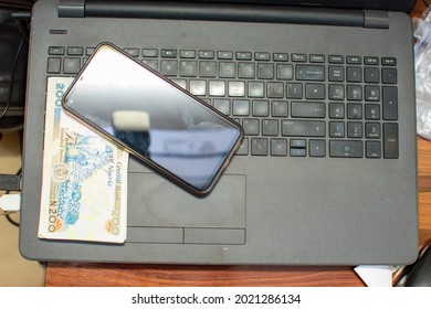 Multiple naira notes, cash or nigerian currency with a smart phone placed on a laptop's keyboard
