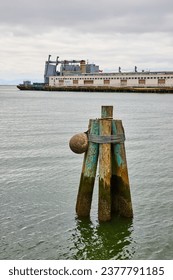 Multiple old worn down pier poles sticking out of water with Pier 40 in background on cloudy day