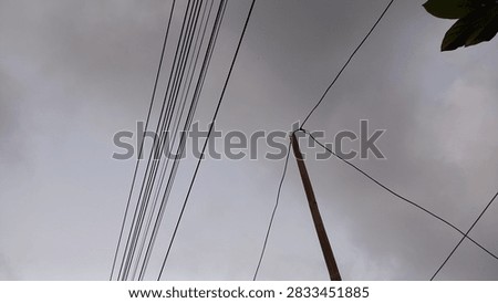 Multiple overhead electrical and communication cables connected to a utility pole, viewed against a cloudy gray sky, representing power infrastructure, telecommunications, and urban or rural utility networks.