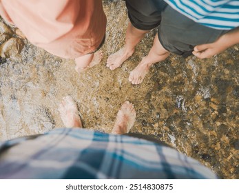 Multiple pairs of bare feet stand in a shallow, clear stream, surrounded by smooth pebbles and flowing water. The image captures a moment of simple joy and connection with nature,  - Powered by Shutterstock