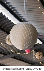 Multiple Paper Lanterns Hanging From The Ceiling Structure With Small Fairy Lights In The Background. Wedding Party Decoration. 