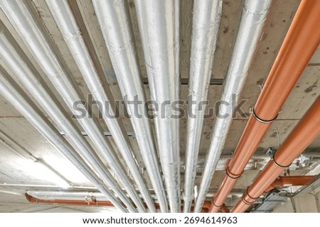 Multiple parallel metal pipes mounted on a ceiling creating an industrial pattern. Building services and infrastructure detail.