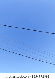Multiple parallel power lines cut sharply across a brilliant, unblemished blue sky, forming a striking pattern of human connection against nature's vastness.
