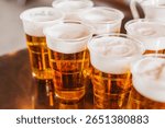 Multiple plastic cups filled with beer. Fresh foam on top of golden lager. Refreshing cold drinks for party or event. Alcoholic beverage on metal table. Social gathering with light beer served.