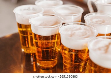 Multiple plastic cups filled with beer. Fresh foam on top of golden lager. Refreshing cold drinks for party or event. Alcoholic beverage on metal table. Social gathering with light beer served.
